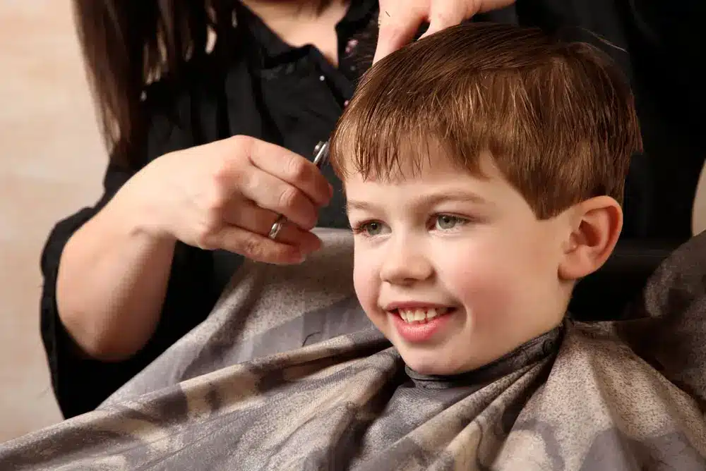 Young Barber Drying Hair of Little Boy Sitting in Barber Shop